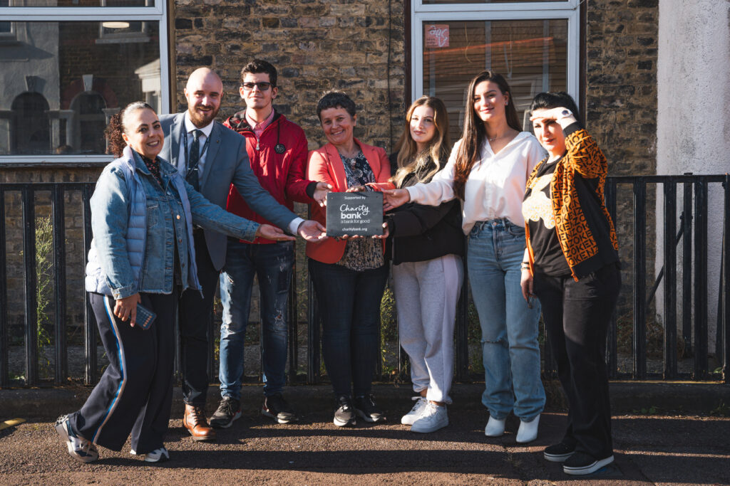 Shpresa team holding charity bank plaque outside building group shot